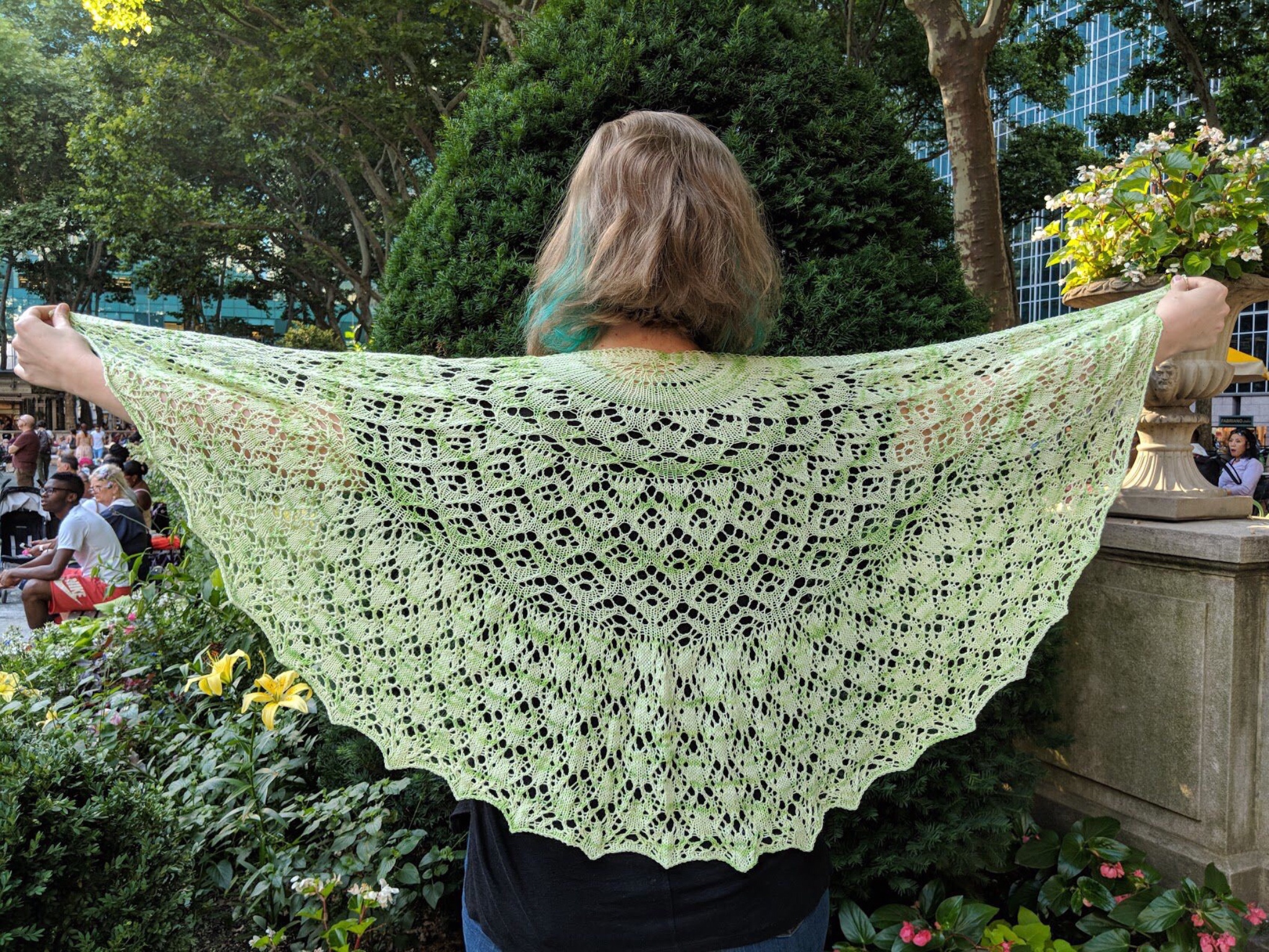 A green semicircular lace shawl being held up over the back of someone’s shoulders 